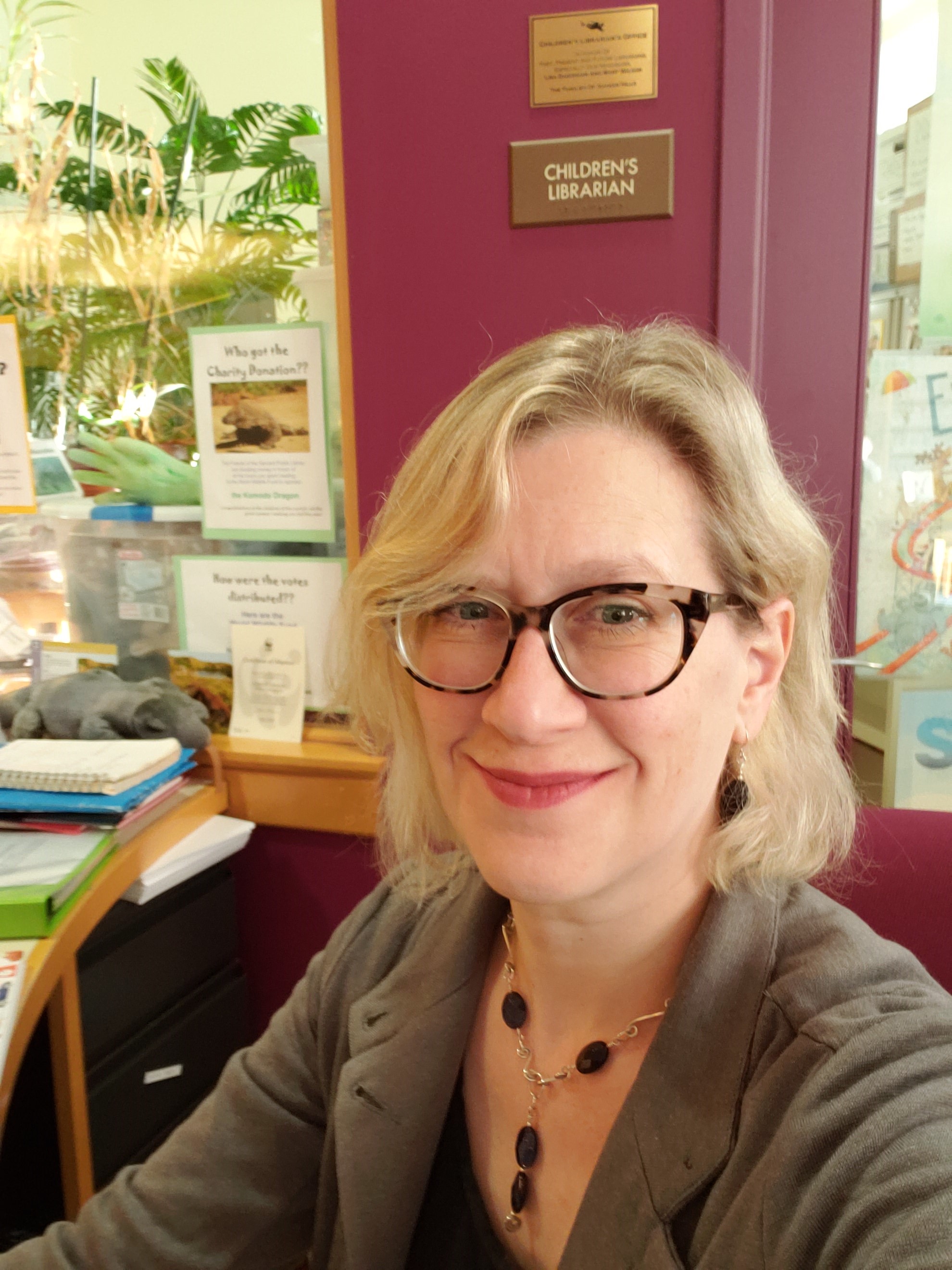 Abby Kingsbury sitting at her desk in front of sign that says Children's Librarian